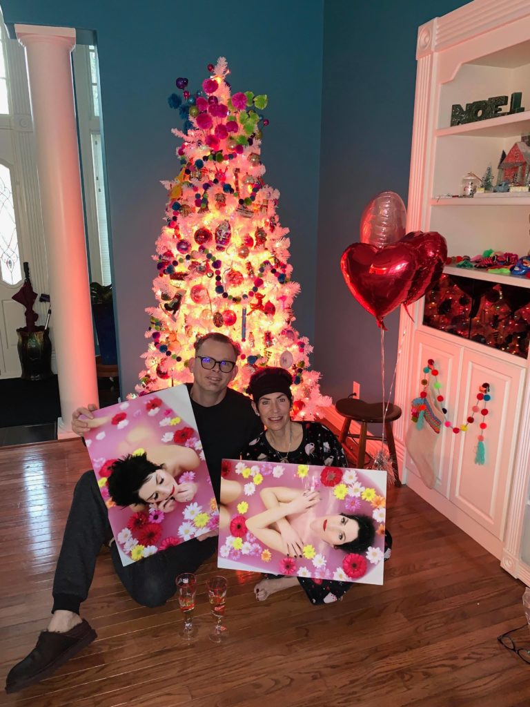 woman posing with her husband holding her wall art frames from her boudoir shoot at UNVEILED studio