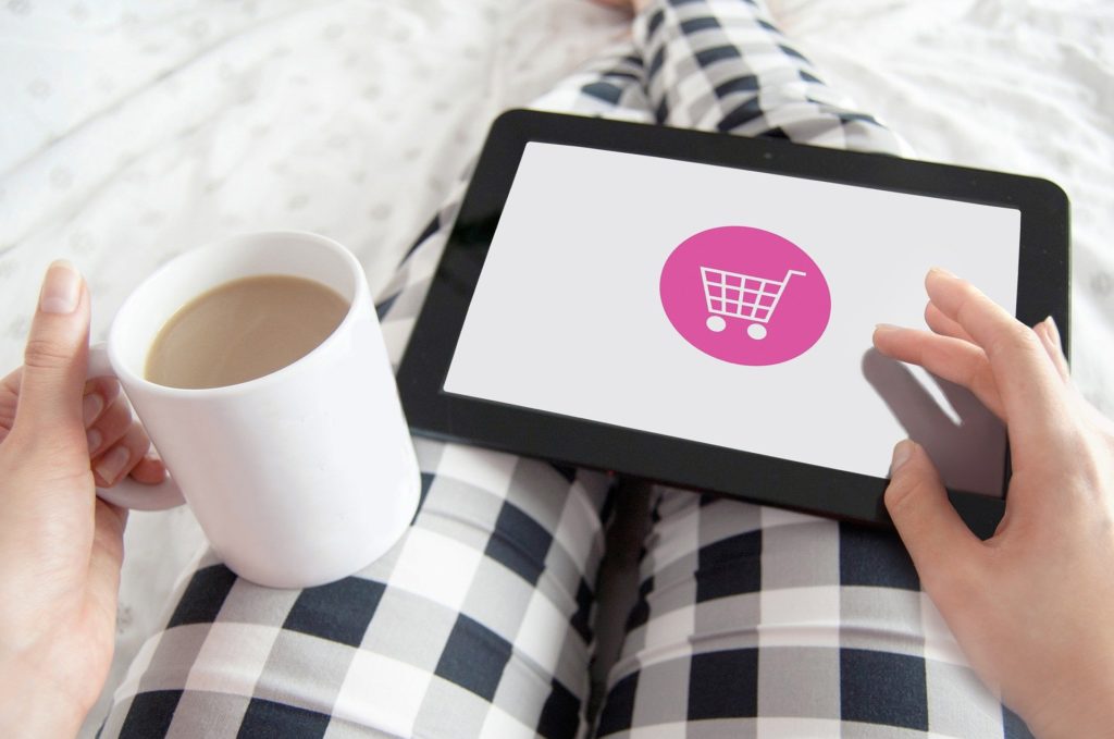 graphic of a person holding a coffee mug and a tablet with the image of a shopping cart on it